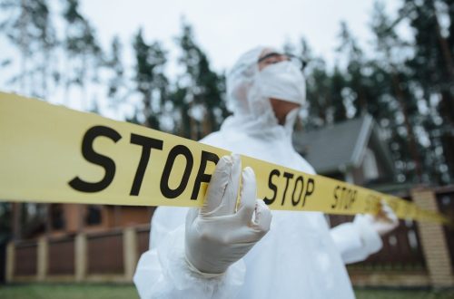 Investigator in protective gear securing crime scene with stop tape outdoors.