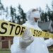 Investigator in protective gear securing crime scene with stop tape outdoors.
