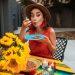 A Hispanic woman savoring a plate of beans in a vibrant outdoor setting with sunflowers.