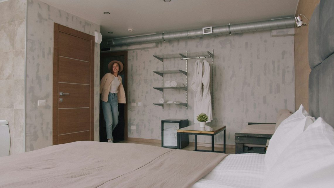 A woman in a hat and jacket entering a modern hotel room